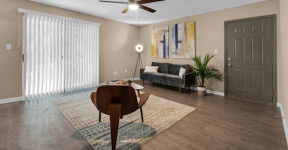 A furnished living room with a sliding door, ceiling fan, and wood flooring at Crystal Lake in Pensacola, Florida.
