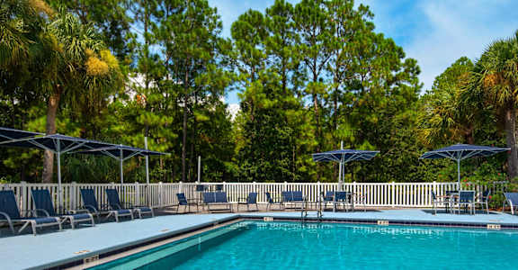 An outdoor swimming pool surrounded by lounge chairs and umbrellas at Crystal Lake in Pensacola, Florida.