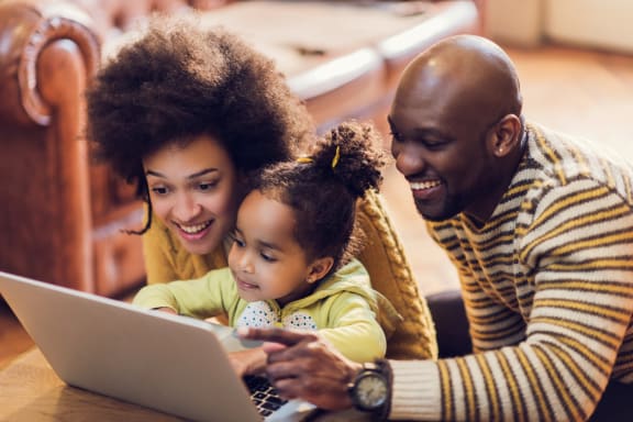 a family of three is gathered around a laptop computer