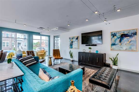 A living room with a blue couch and a black leather ottoman.
