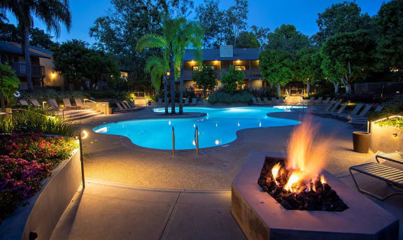 a swimming pool at night with a fire pit
