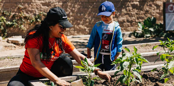 A woman and a boy are planting a tree in a garden.