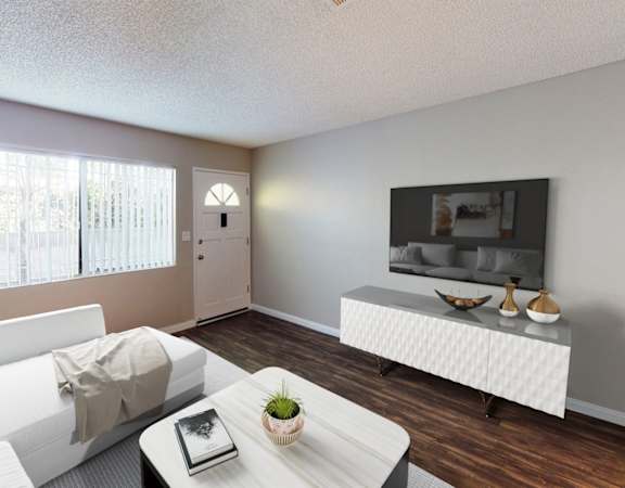 A living room with a white couch, a coffee table, and a flat screen TV mounted on the wall.