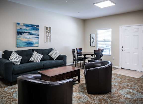 A living room with a black couch and a painting on the wall.