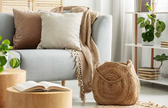A grey couch with a pillow and a small table with a plant and a picture frame.