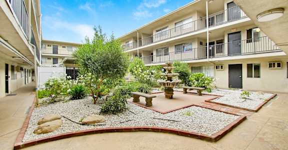 a courtyard with a fountain and benches in front of an apartment building