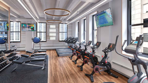 Gym at The Gio Apartments with rows of exercise equipment and a TV.