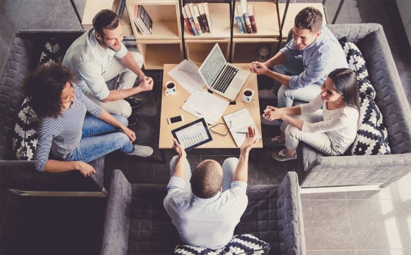 a group of people sitting around a table with their laptops