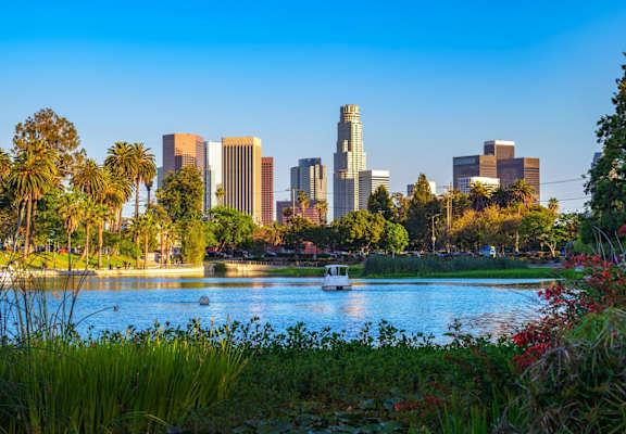 A city skyline is seen from a park with a body of water in the foreground.