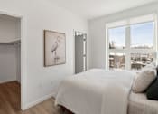 Thumbnail 2 of 51 - A bedroom with a bed, a painting of a bird, and a view of the outside through a window.