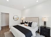 Thumbnail 24 of 51 - A bedroom with a large bed, a round mirror, and a nightstand with a lamp.
