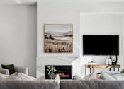 Thumbnail 21 of 51 - A living room with a grey couch, a fireplace, and a painting on the wall.