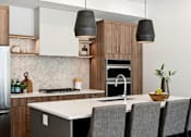 Thumbnail 20 of 51 - A modern kitchen with a white countertop and grey chairs.