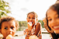 Three children eating ice cream in a sunny outdoor setting.