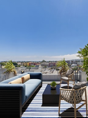 A patio with a blue couch and a chair with a table and potted plant.