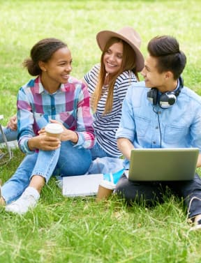 three women sitting on the grass with a laptop