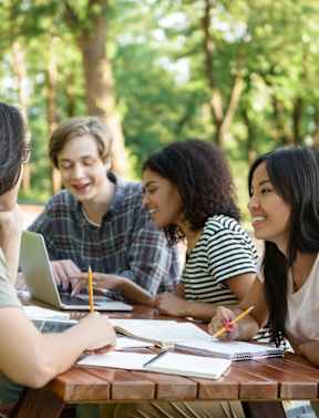 Four people studying outdoors at a picnic table.