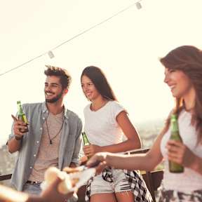 Four friends toasting with beer bottles on a rooftop.