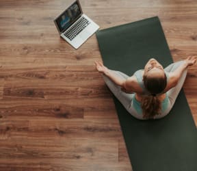 a woman sitting on a yoga mat with a laptop on the table