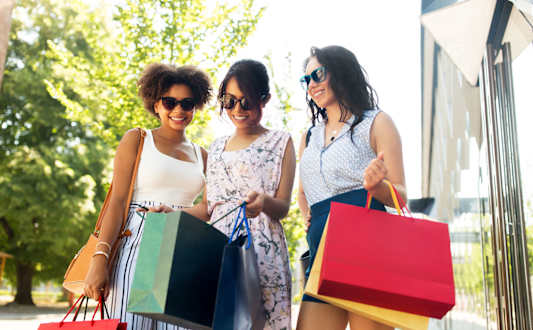 Three women are standing together holding shopping bags.