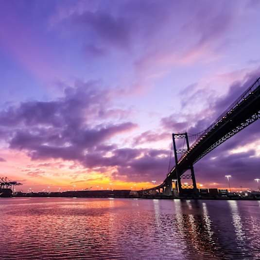 A bridge spans across a calm body of water under a vibrant sunset sky.