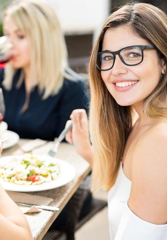 Three people are sitting at a table eating and drinking wine.