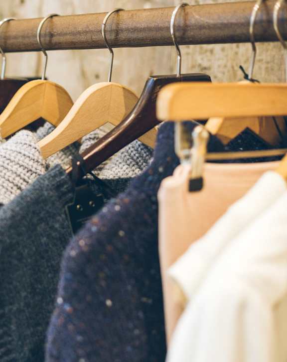 A row of sweaters hang on wooden hangers.
