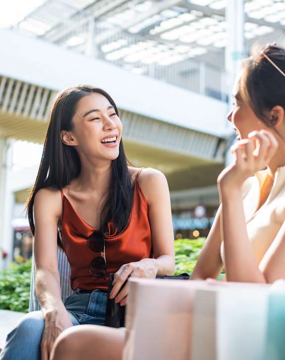 Two women are sitting and talking in a brightly lit outdoor area.