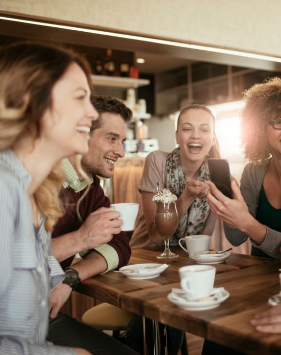 a group of people sitting around a table drinking coffee and looking at a cell phone