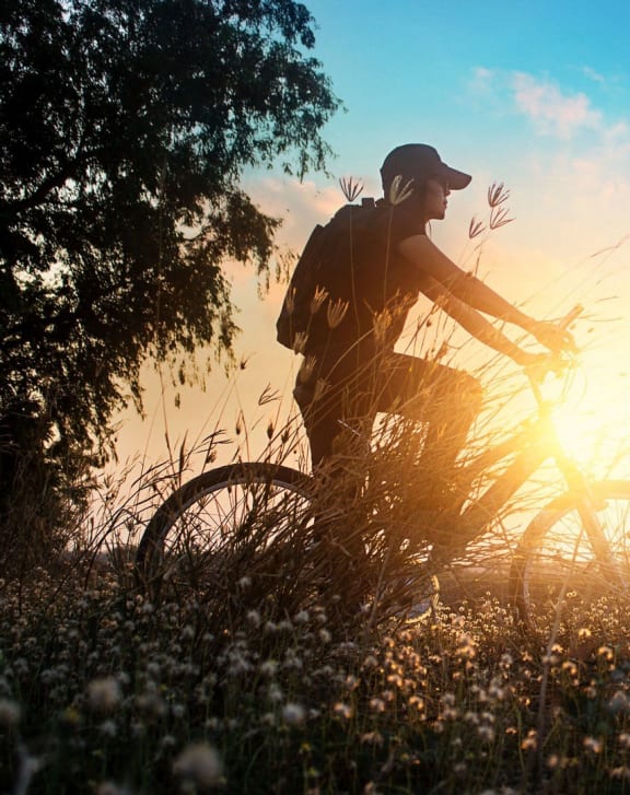 a man riding a bike in a field with the sun behind him