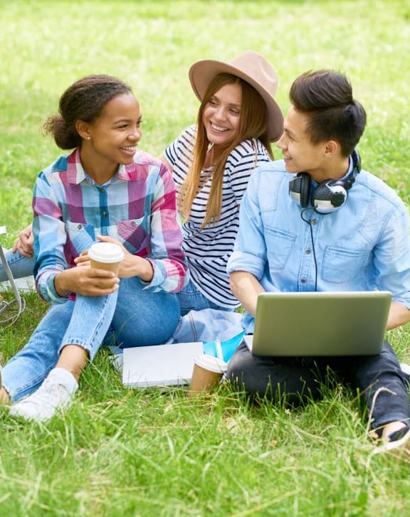 three women sitting on the grass with a laptop
