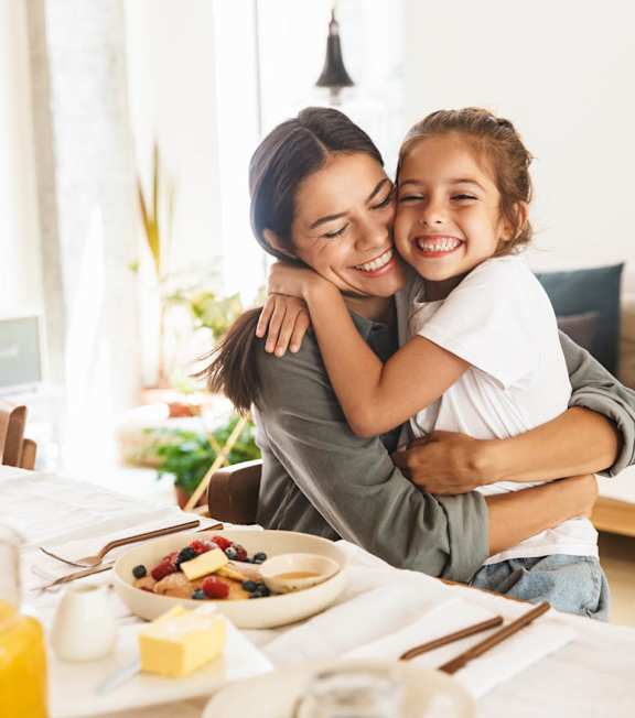 A woman and a child are hugging at a breakfast table.