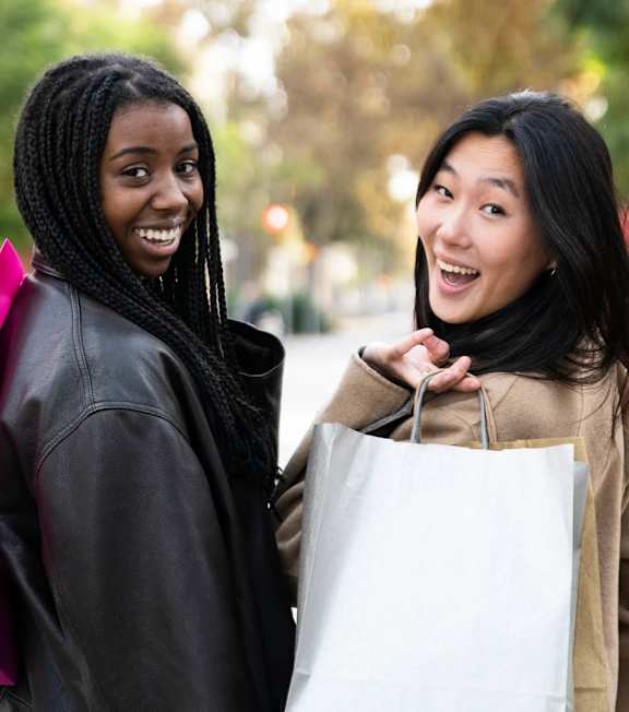 Two women are standing together holding shopping bags.