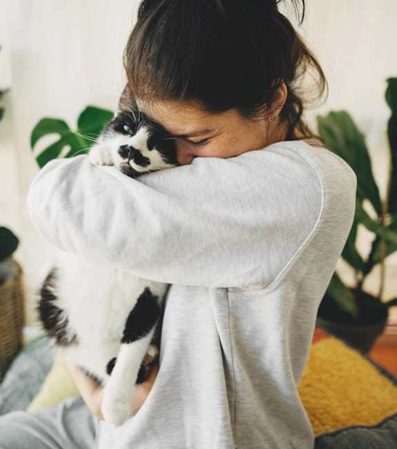 A woman is hugging a cat in a room with plants.
