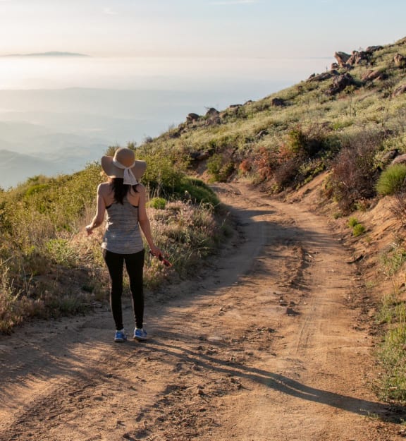 a woman walking down a dirt road with a hat on her head
