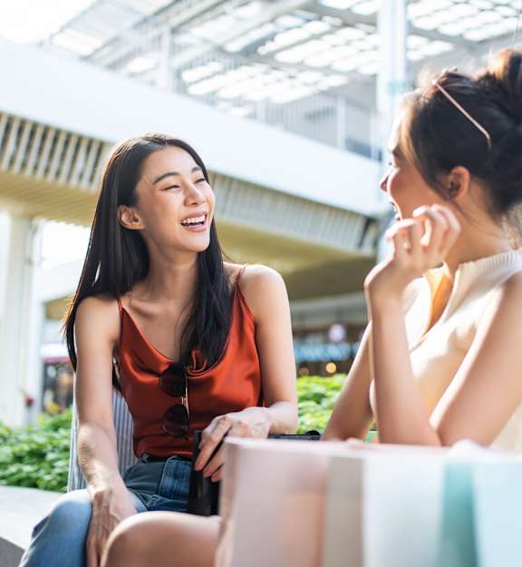 Two women are sitting and talking in a brightly lit outdoor area.