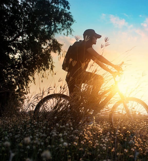 a man riding a bike in a field with the sun behind him