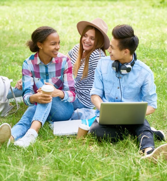 three women sitting on the grass with a laptop