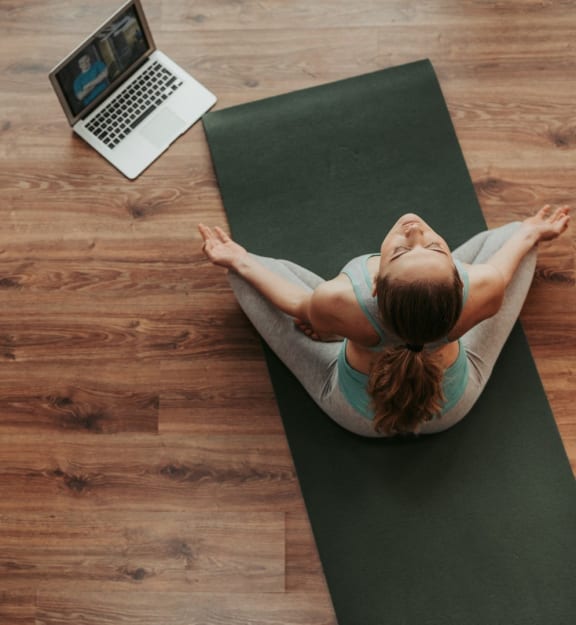 a woman sitting on a yoga mat with a laptop on the table