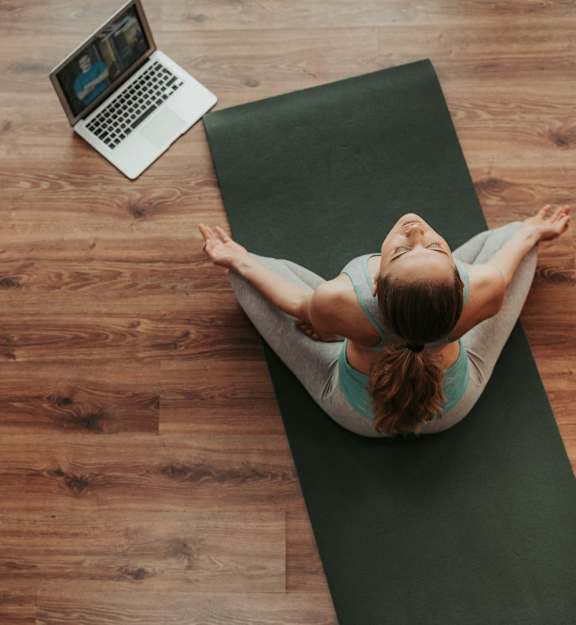 a woman sitting on a yoga mat with a laptop on the table