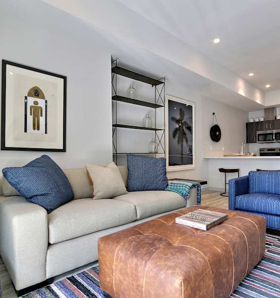 A living room with a white couch and a brown leather ottoman.