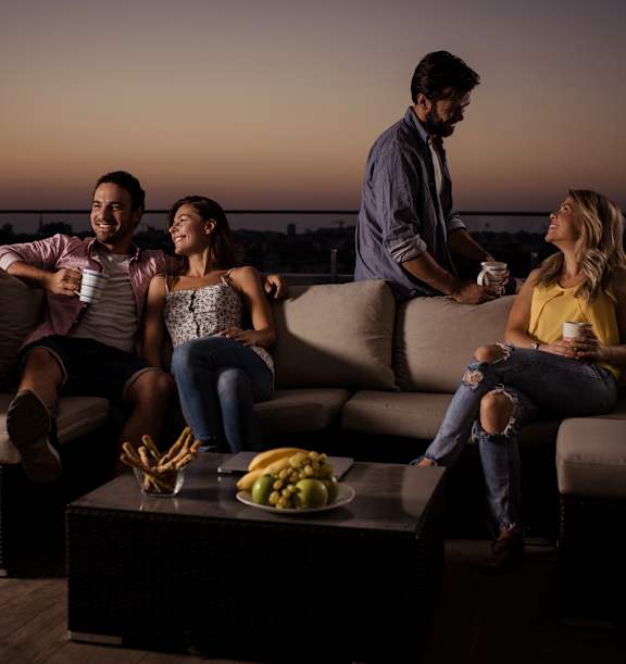Four people sitting on a couch with a man standing and holding a tray of food.