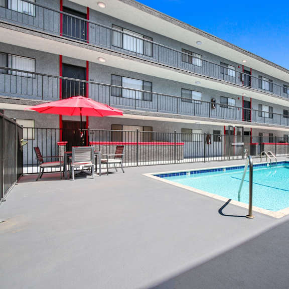 A swimming pool is surrounded by a patio with chairs and umbrellas.