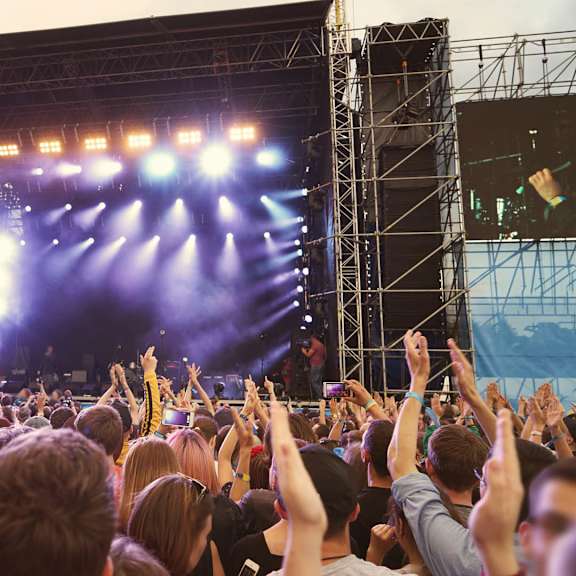 A crowd of people at a concert with their hands raised in the air.