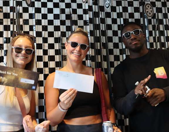 Three people holding cards and a can in front of a checkered wall.