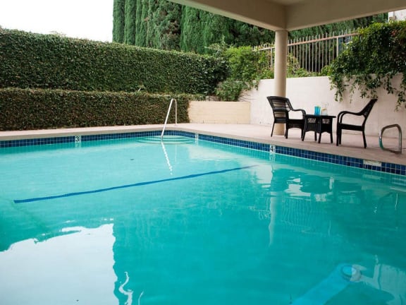 the pool is next to a patio with chairs and a table