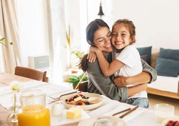 A woman and a child are hugging at a breakfast table.
