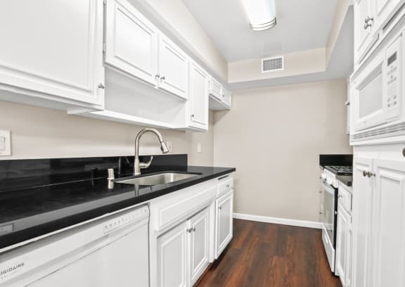 a kitchen with white cabinets and black counter tops and a sink