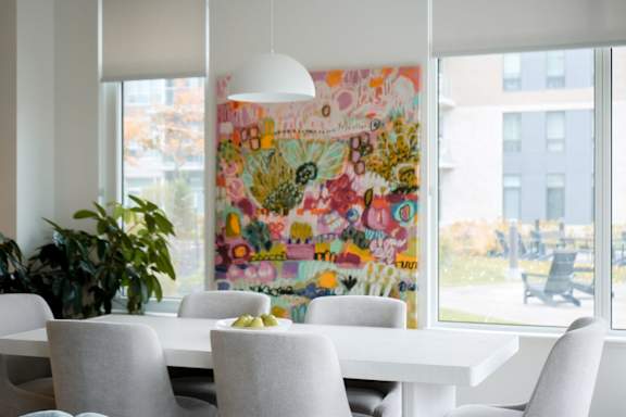 A white dining table with six chairs and a large, colorful painting on the wall. at Petries Landing I Apartments , Ontario