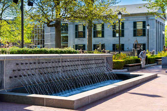 A water fountain in front of a building with people walking by.